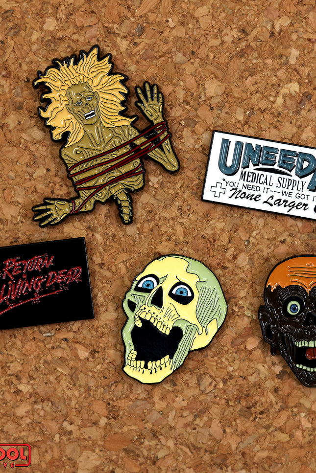 Top view of the Return of the Living Dead enamel pins featuring the skeleton head, Tarman head, Half-corpse, Uneeda Medical Supply logo, and The Return of The Living Dead Logo.