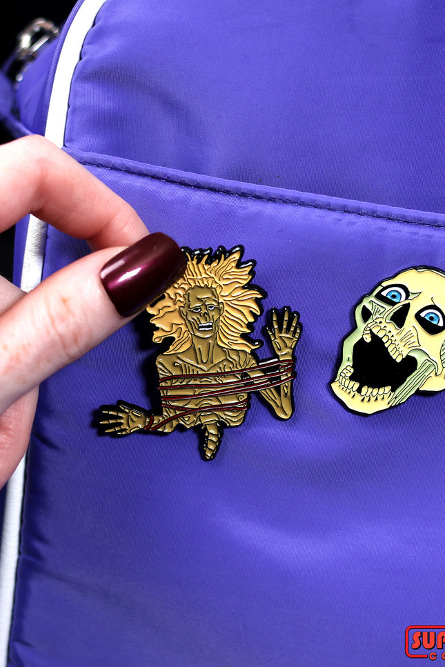 Enamel pins of a half-corpse and skeleton head pinned on a purple bag.